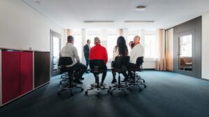En grupp människor sitter på stolar i en ring i kontorsmiljö.