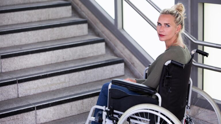 Kvinna i rullstol nedanför en trappa.