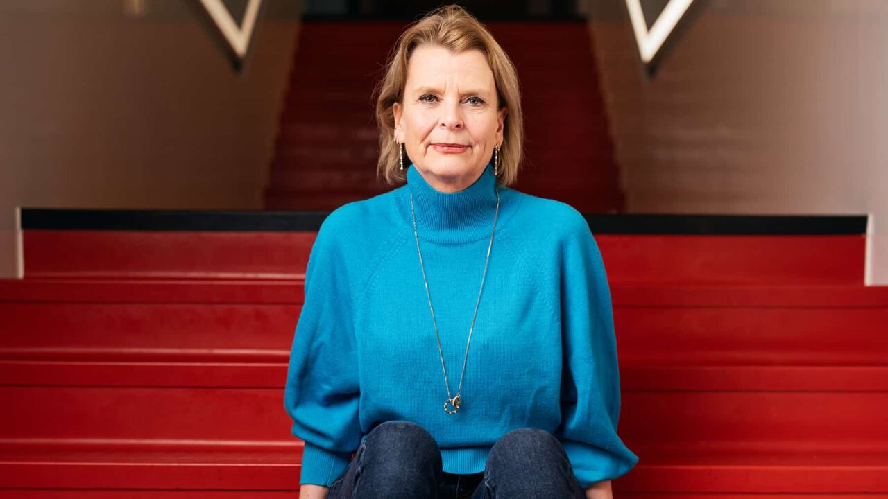Åsa Regnér i blå polotröja sitter på en röd trappa och tittar rakt fram.