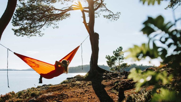 person som ligger i hängmatta och tittar ut över vattnet
