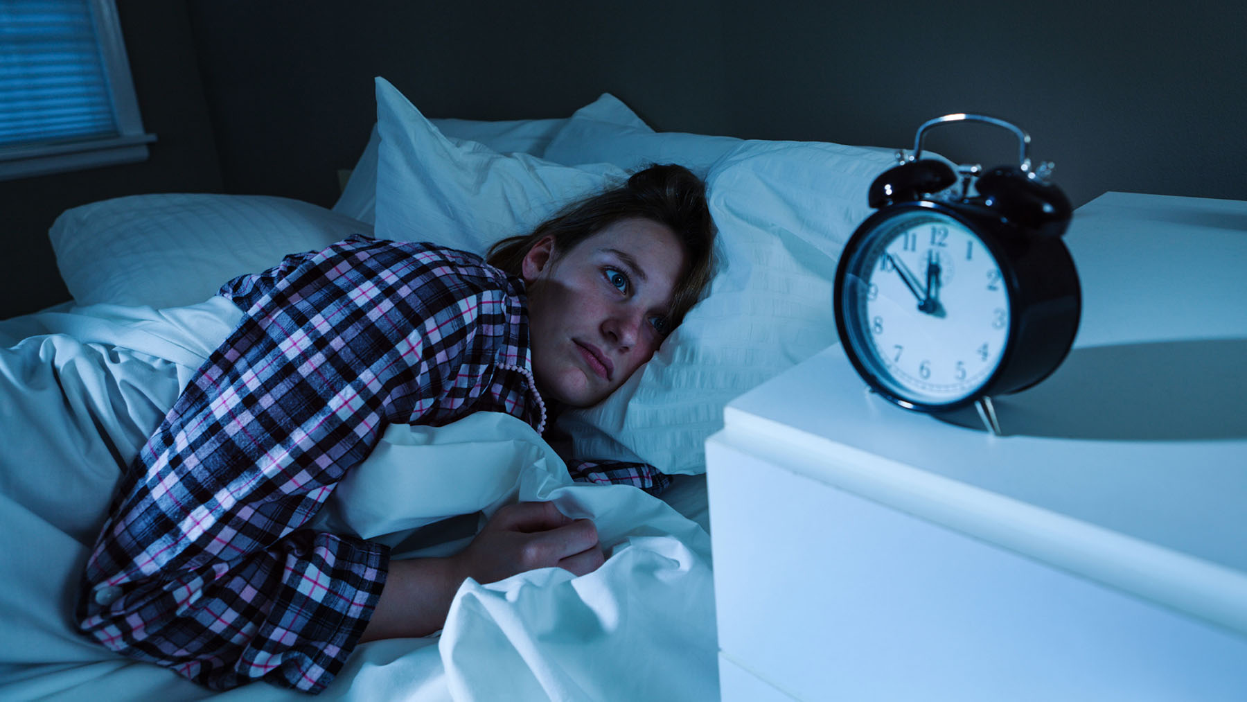 Kvinna som ligger sömnlös på natten och tittar mot väckarklockan.
