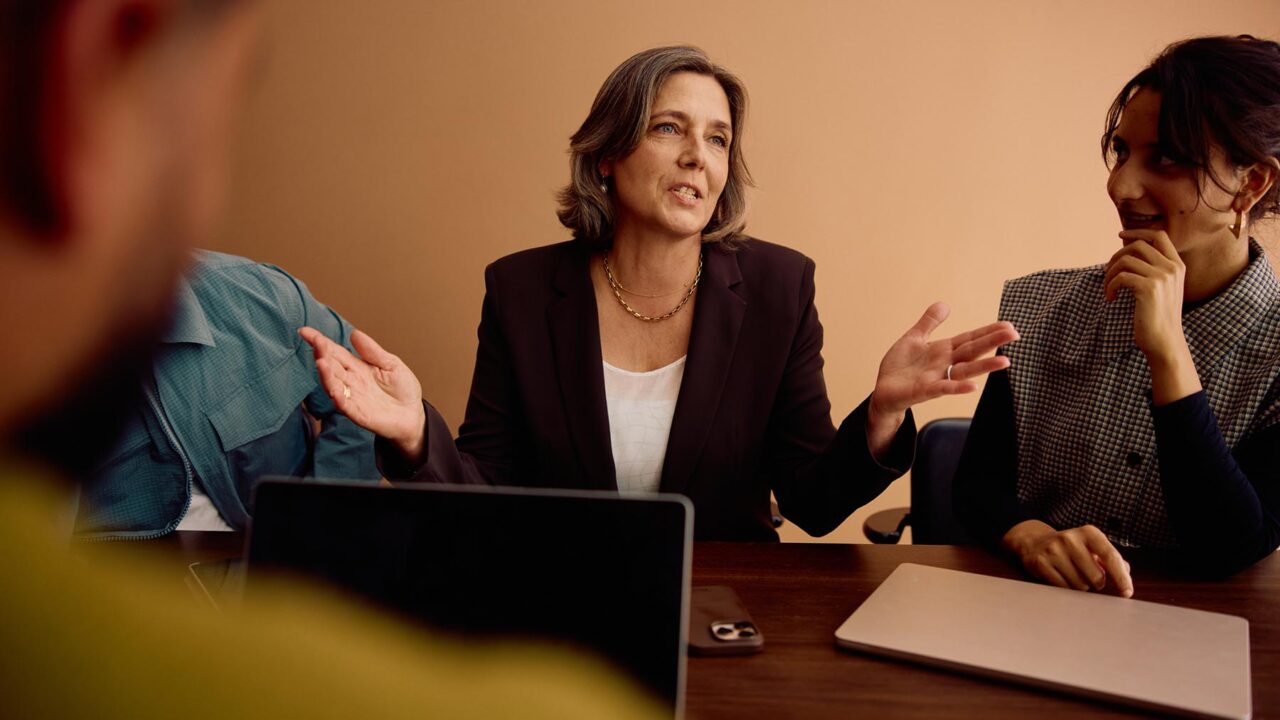 En kvinna vid konferensbord gestikulerar med händerna.