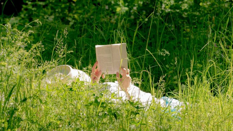 Person ligger avslappnad i gräset och läser en bok.