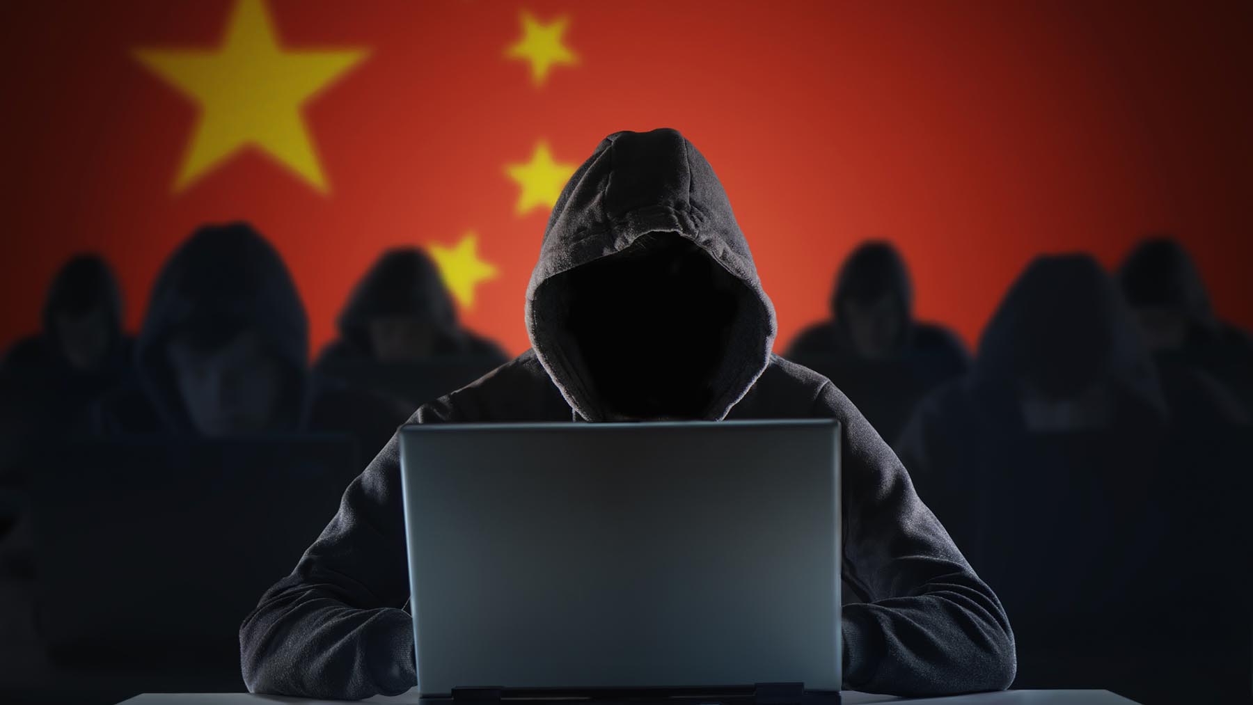 Cyberbrottsling i huva framför en laptop, i bakgrunden många fler och en stor kinesisk flagga.