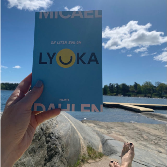 Ninas hand som håller i en bok av Micael Dahlen vid en strand .