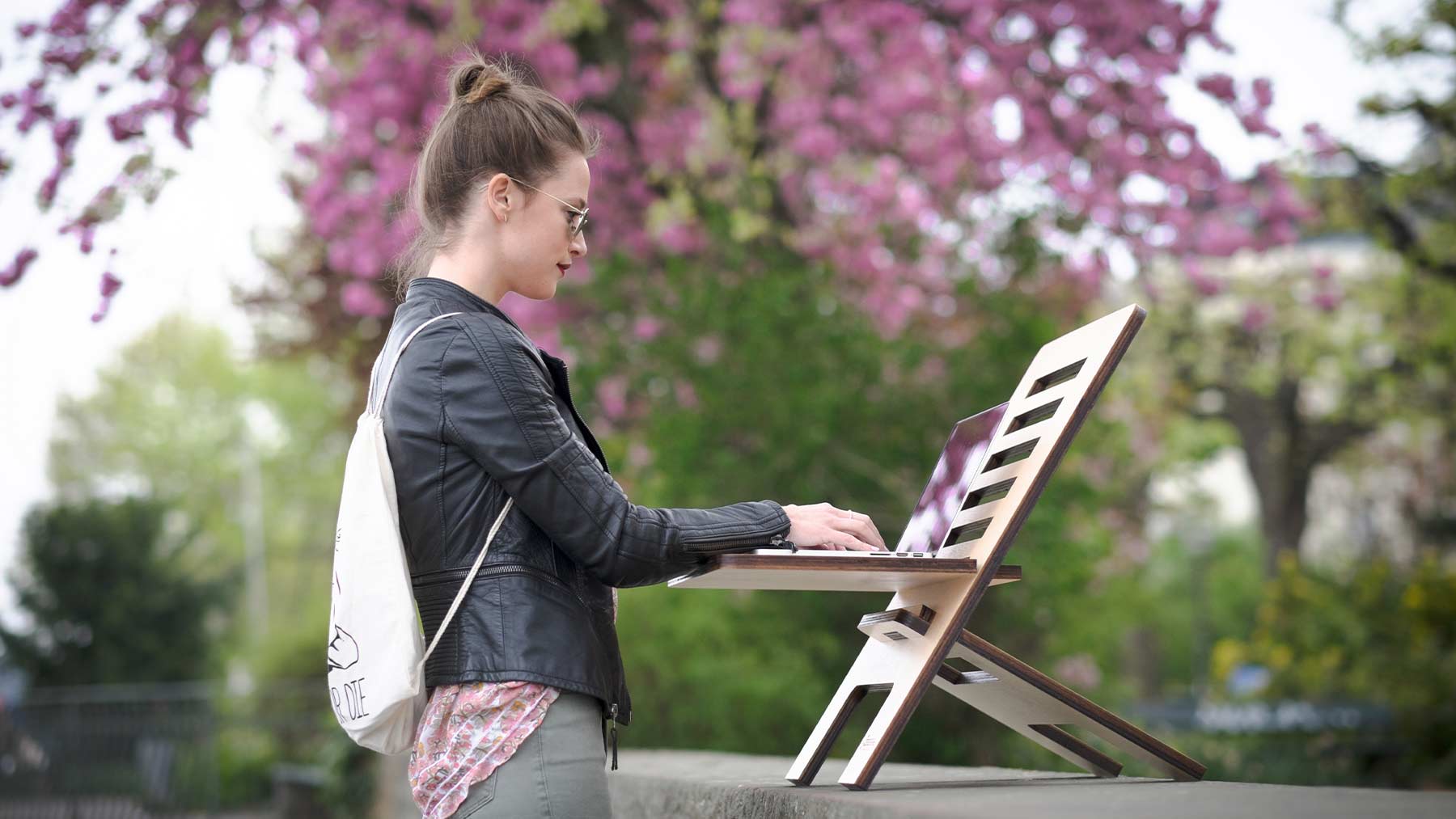 En ung kvinna står upp och jobbar utomhus med en dator framför sig.