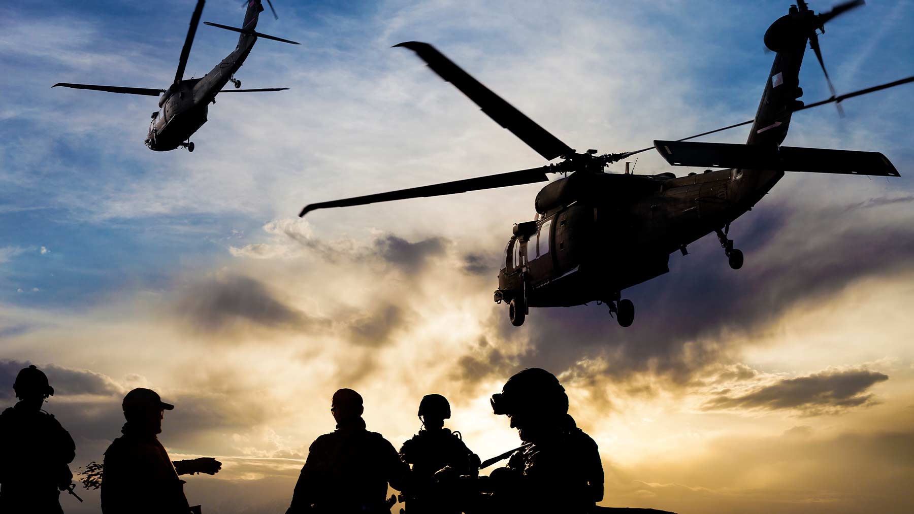 En militär operation med soldater och helikoptrar i luften i skymningen.