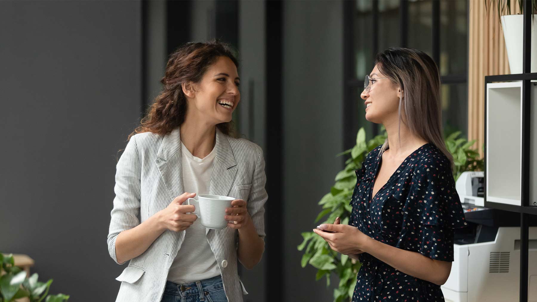 Två kvinnor på ett kontor pratar med varandra och ler.