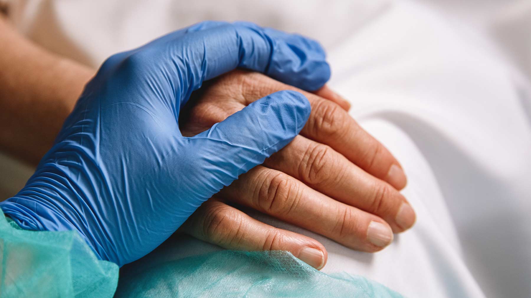 En bild på två händer. En läkare har lagt sin hand över en patients hand, i en tröstande gest.