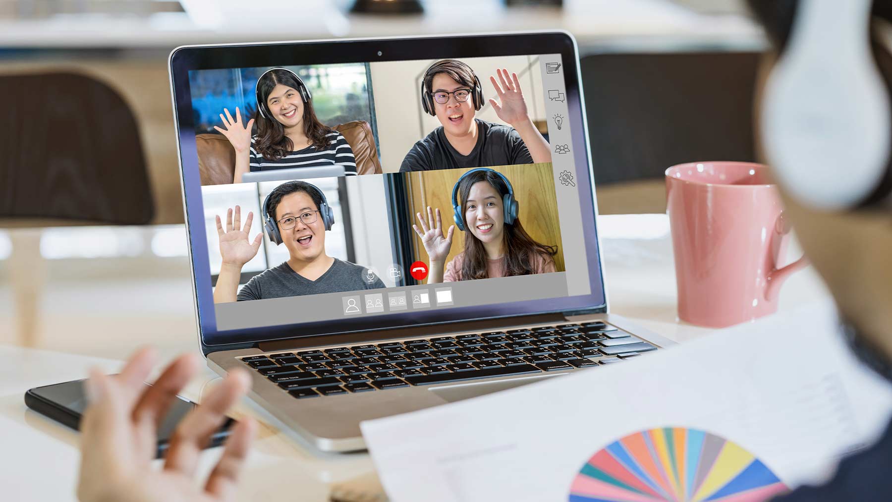 Fyra unga medarbetare syns i rutor på en dator under ett digitalt möte. De vinkar till varandra.
