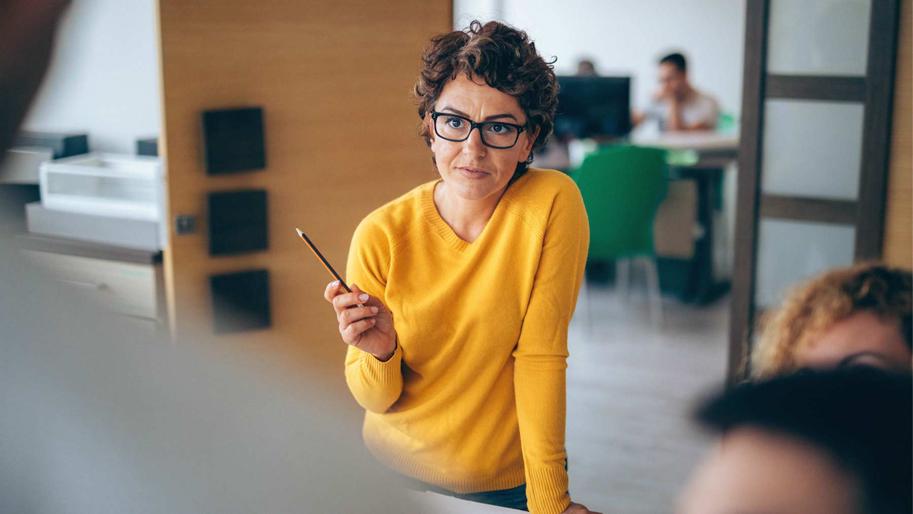 Bild på kvinna med gul tröja och som håller i en penna.